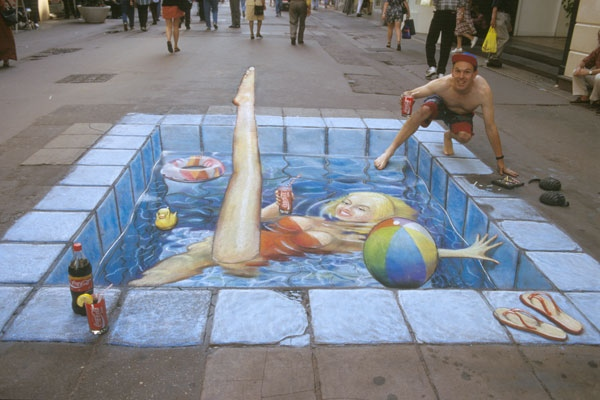 A pavement painting of a swimming pool with a person sitting at its edge, seen from the illusion’s convincing viewpoint.